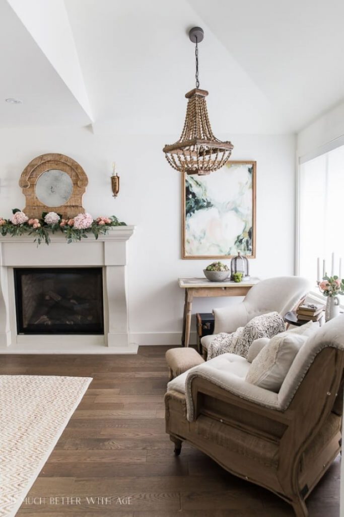 A French farmhouse style living room with vintage french curniture and a mantel covered in pink blooms