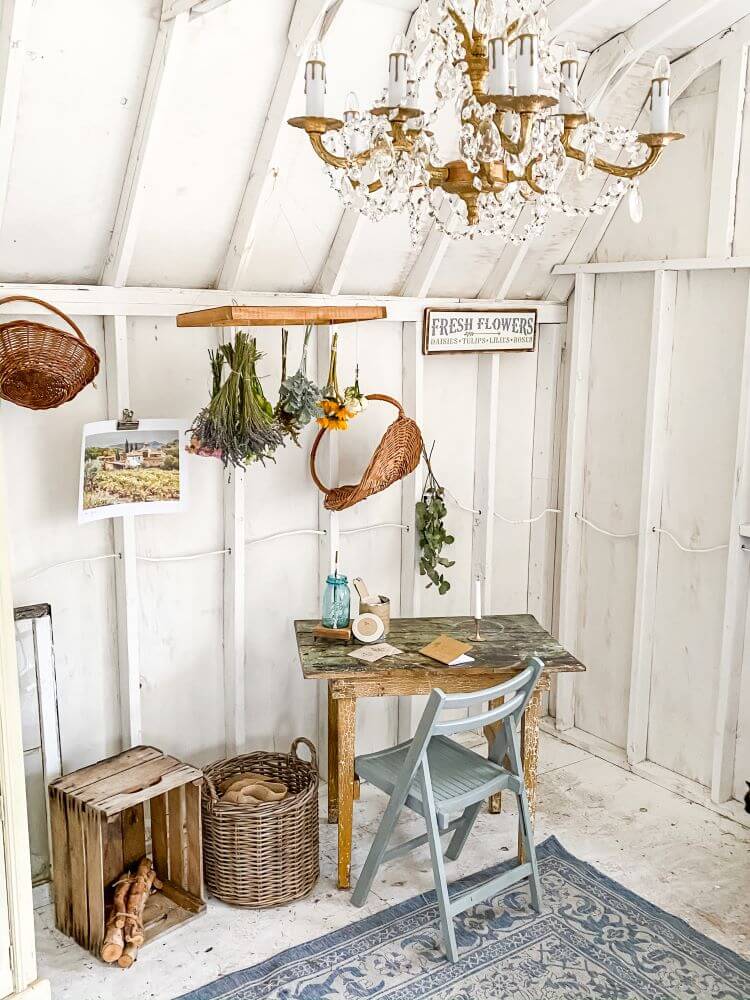 A room with white paneling has a vintage style rug faded in colors of mute blues. Dried flowers and herbs hang in bouquets along the wall paneling for summer decor