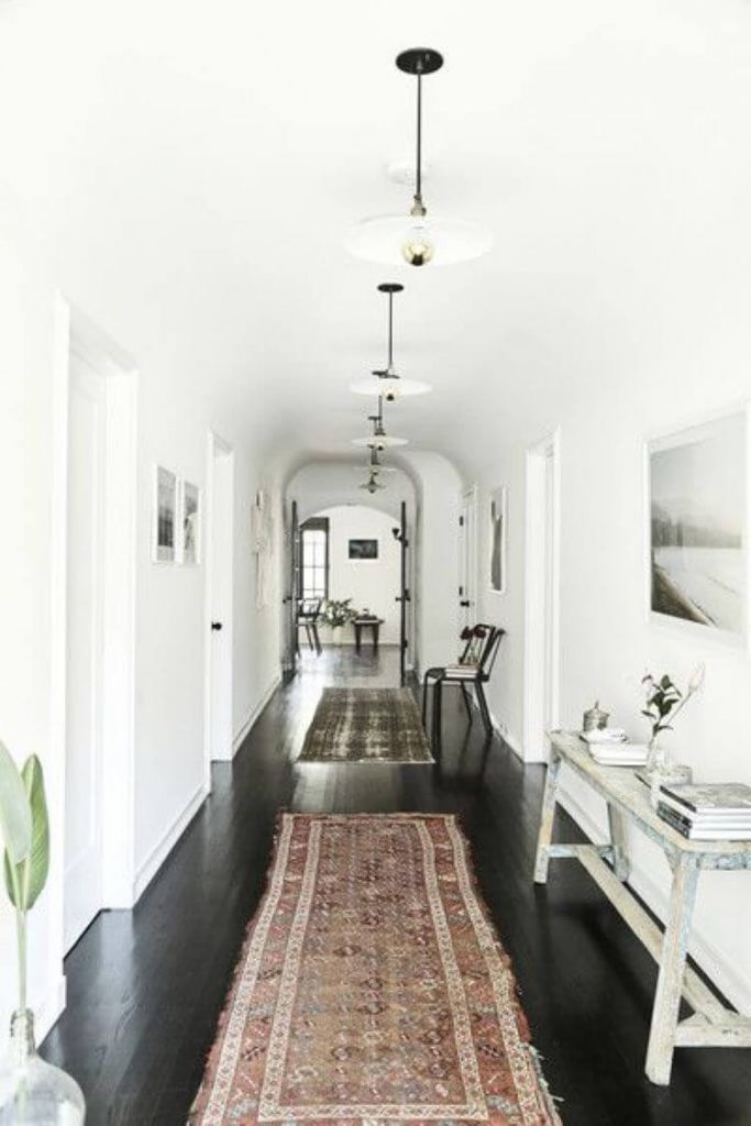 dark wood floor colors in a long hallway with white walls and antique rugs on the floors