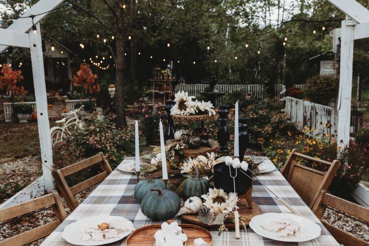 Outside, in the garden, sits a beautiful fall tablescape with dark blue pumpkins and white candles atop a plaid table runner