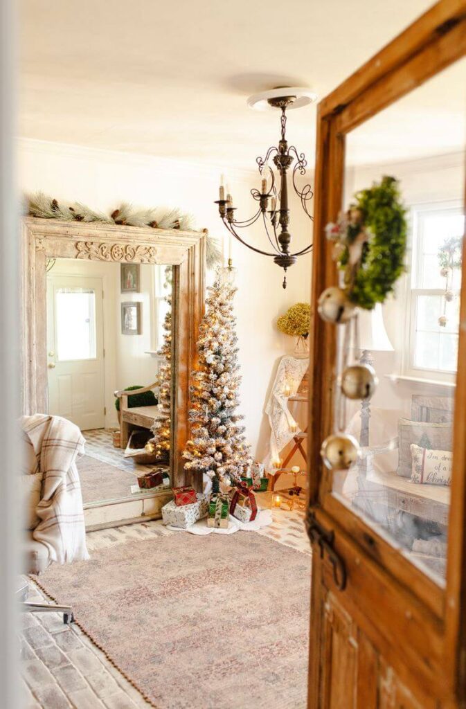 A door opens to frame a view of a room brimming with Christmas décor in the shape of flocked Christmas trees, evergreen swags, and a pile of presents