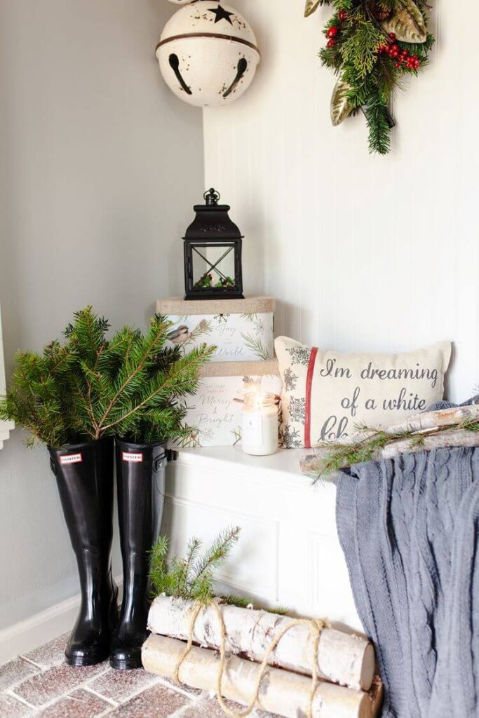 A closeup of the entryway shows the evergreen sprigs tucked in charming rainboots for a farmhouse look