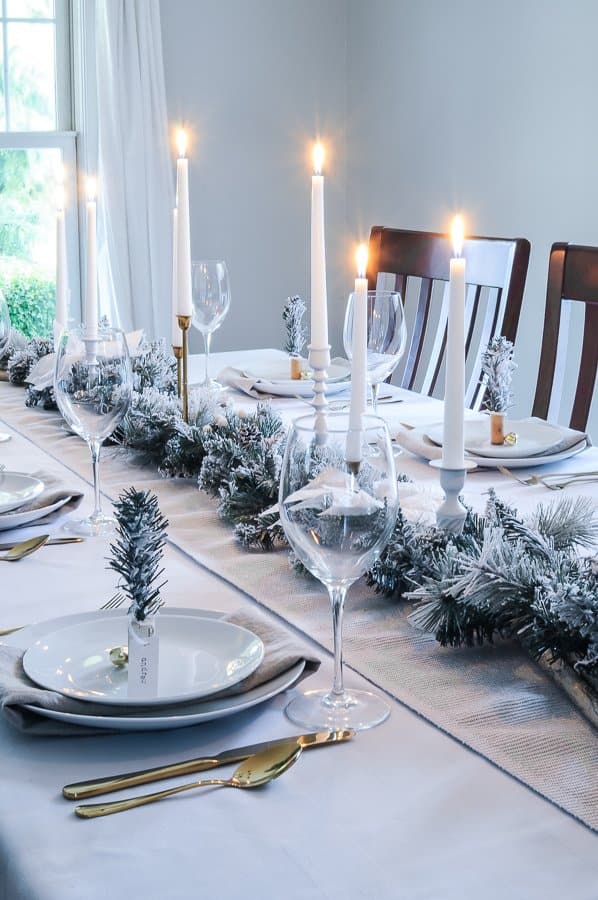 frosty winter tablescape with a simple green garland and white candles with gold cutlery