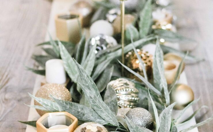 close up of center tablescape full of fresh green garland, gold ornaments, and simple white candles with a white table runner