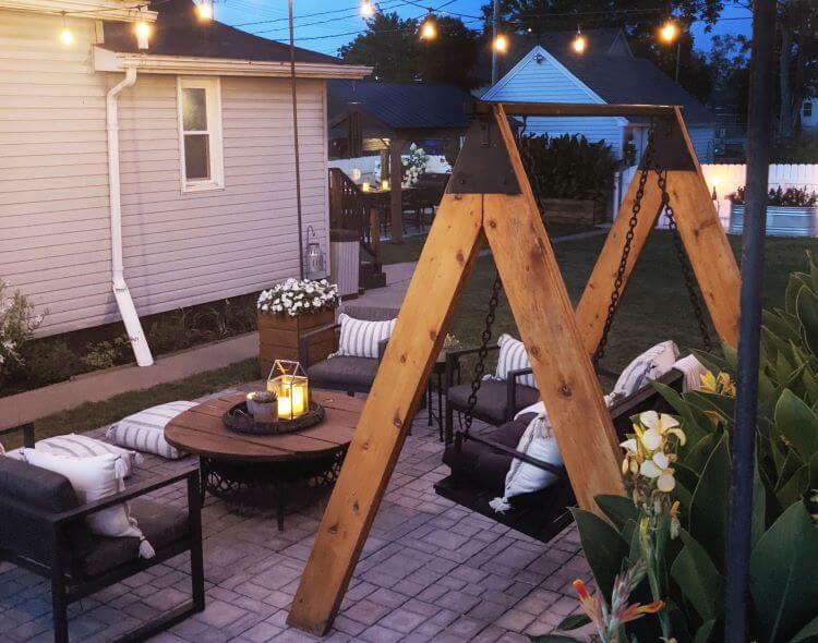 The backyard has been revived after the storm. A cozy sitting area includes a hanging bench and several chairs around a shiplap style outdoor table.