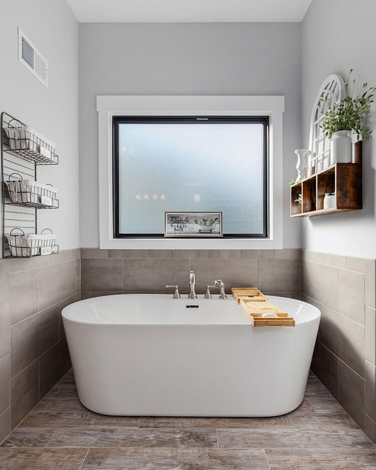 A large cloudy window is made so to obscure the above ground tub surrounded by concrete tiles in the master bathroom