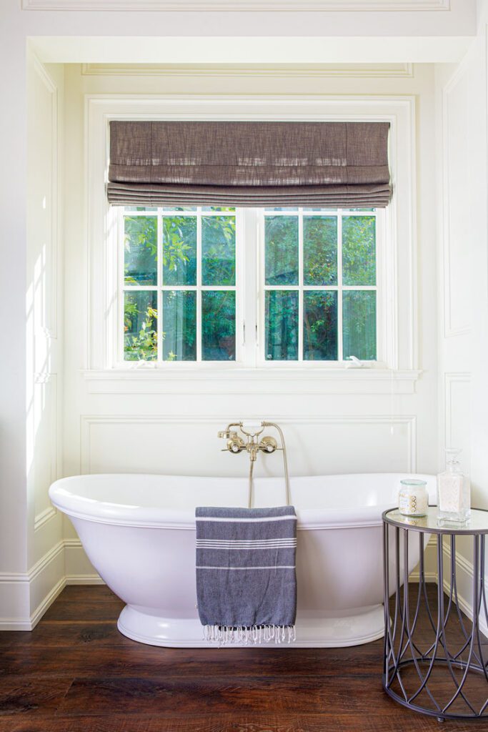 Bathroom in elegant farmhouse with white freestanding tub and wood floors