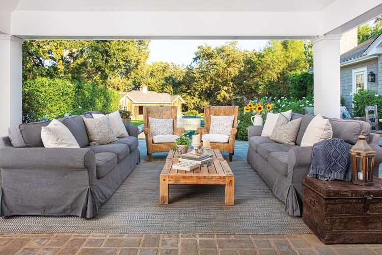 Covered patio outside the family room with gray sofas and wood coffee table in the elegant farmhouse