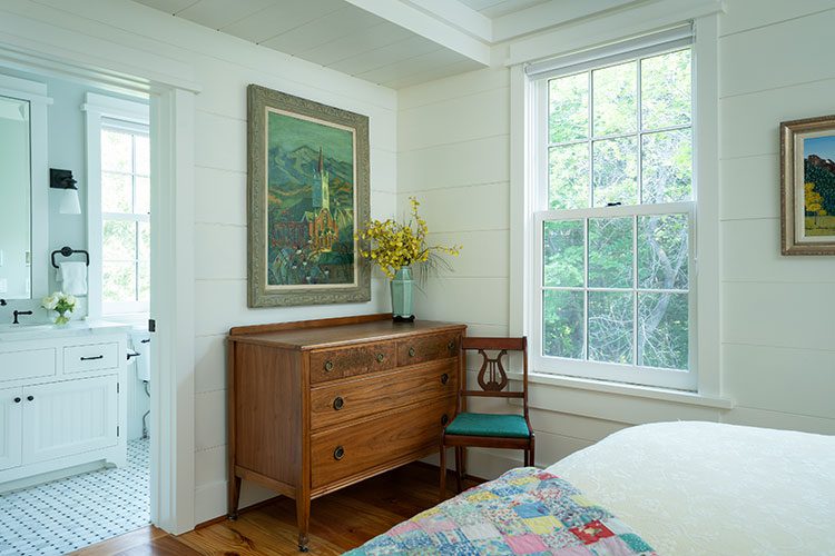 A bedroom with white shiplap working as a blank background uses wood furniture and artwork of provincial themes to set the tone of this farmhouse refresh