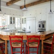 The mostly all white kitchen iis set off by bright red raise bar chairs and wood accents in the surrounding bar countertops framing the kitchen's cooking space in replacement of a traditional kitchen island