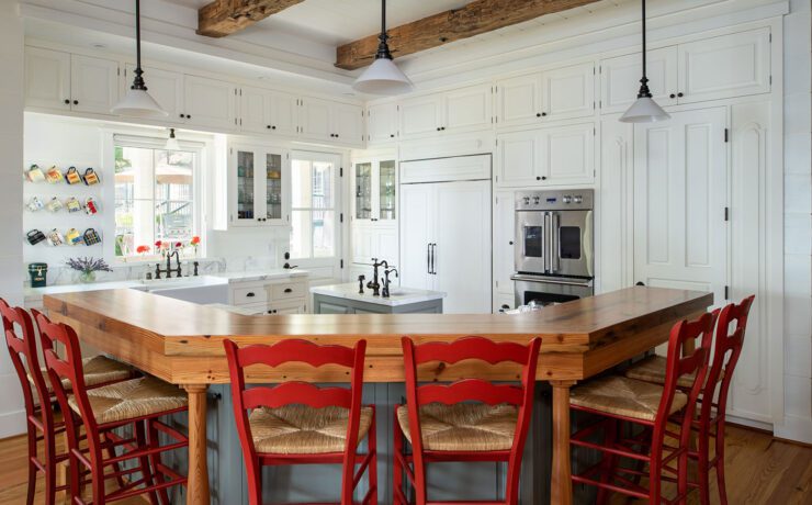 The mostly all white kitchen iis set off by bright red raise bar chairs and wood accents in the surrounding bar countertops framing the kitchen's cooking space in replacement of a traditional kitchen island