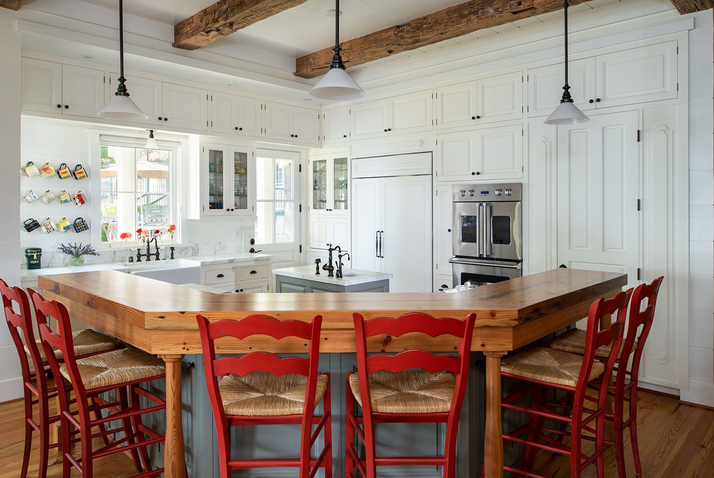 The mostly all white kitchen iis set off by bright red raise bar chairs and wood accents in the surrounding bar countertops framing the kitchen's cooking space in replacement of a traditional kitchen island