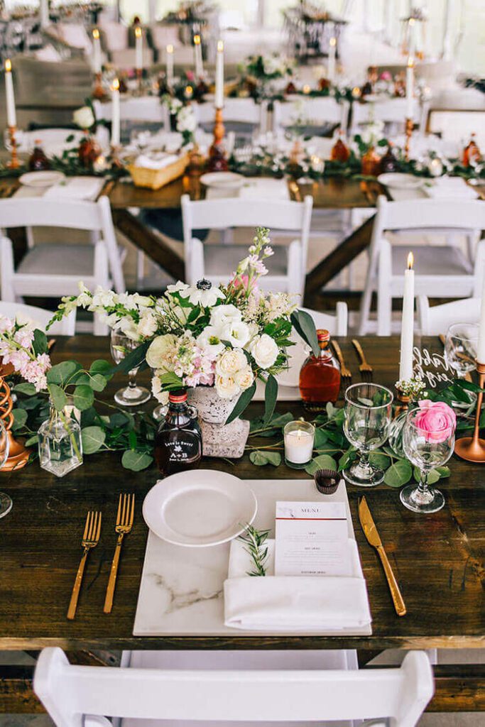 Table setting with flower centerpieces and greenery, candlesticks, and marble place settings.