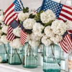 Blue mason jars on a shelf with white flowers and mini American flags.