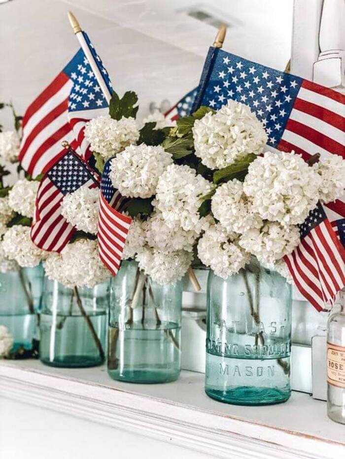 Blue mason jars on a shelf with white flowers and mini American flags.