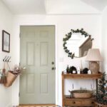 This entryway features a sage green front door with tiled flooring and a wooden side table with boho decor.