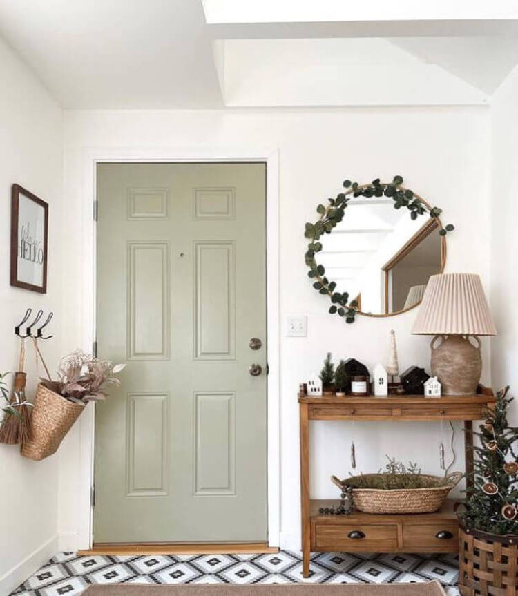 This entryway features a sage green front door with tiled flooring and a wooden side table with boho decor.