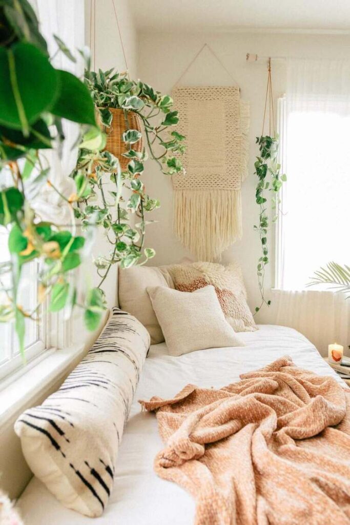 A boho bedroom with cream throw pillows and hanging plants.
