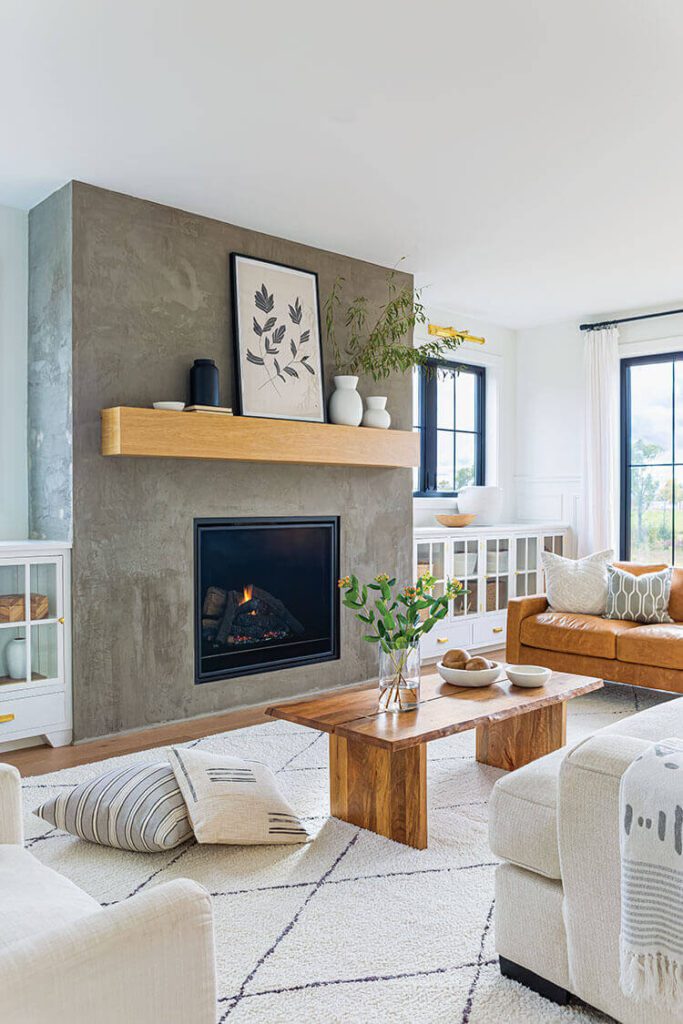 This living room has natural textures and colors like the concrete fireplace, wooden coffee table, and brown leather couch.