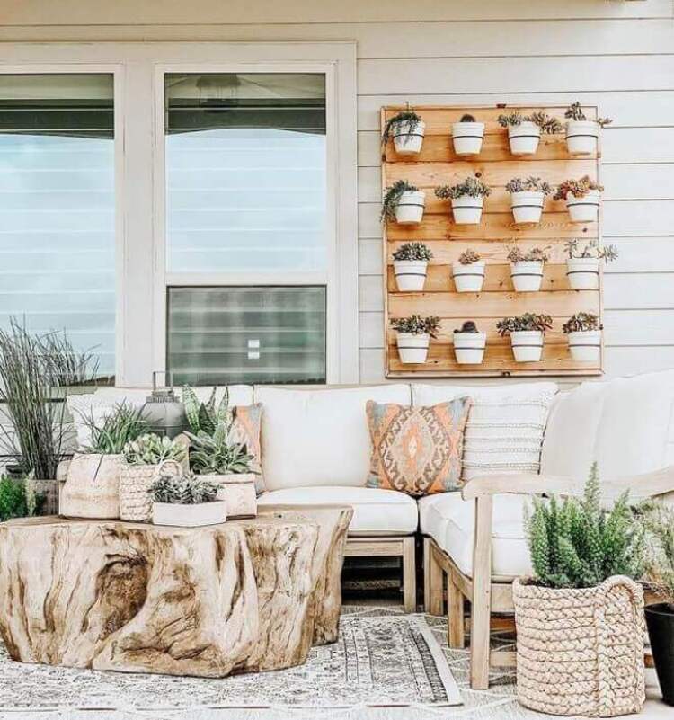 An outside patio with white furniture and tree stump table, with a board of hanging plants.