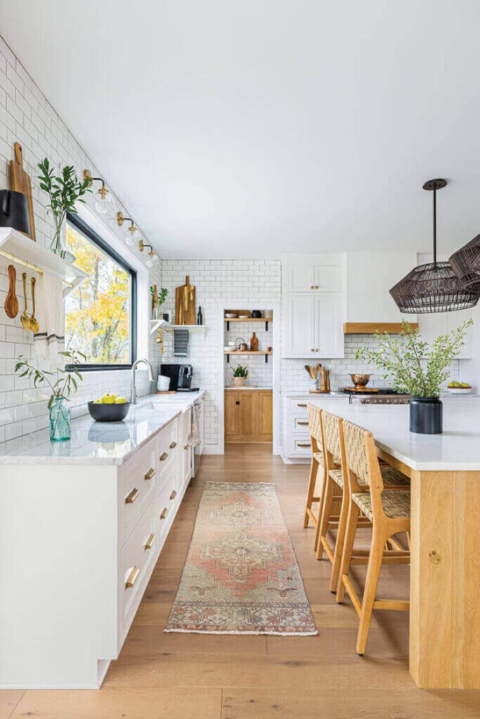 This kitchen has white cabinets and white brick walls, with an oak island and a pink bohemian runner.