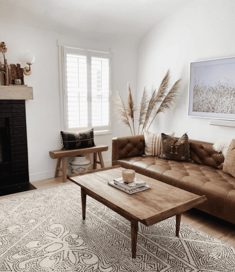 A brown leather couch paired with tan throw pillows and coffee table, highlighted by a textured rug.