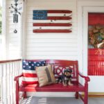 4th of July porch set up with red front door and bench and American flag wooden sign.