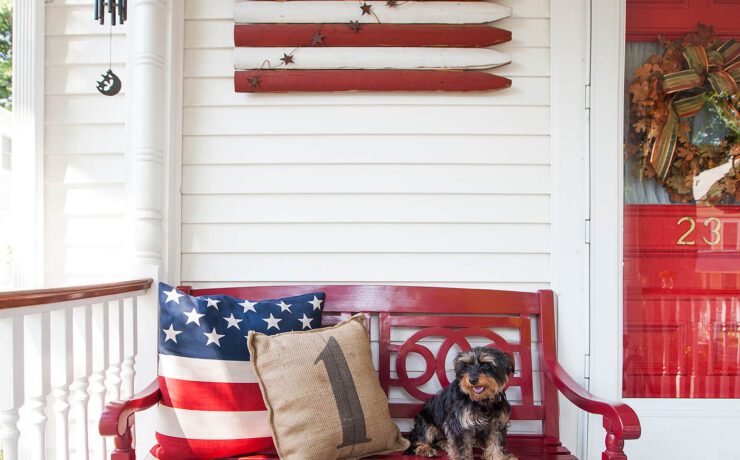 4th of July porch set up with red front door and bench and American flag wooden sign.