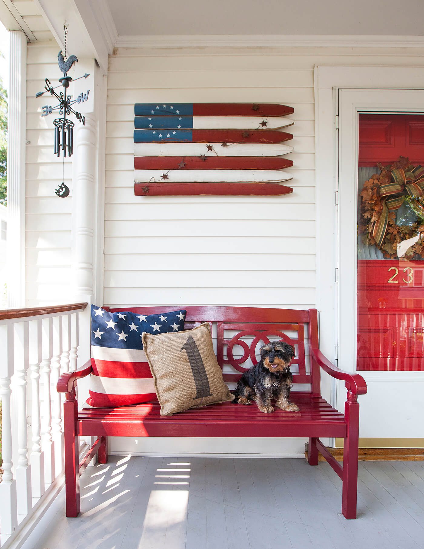 4th of July porch set up with red front door and bench and American flag wooden sign.