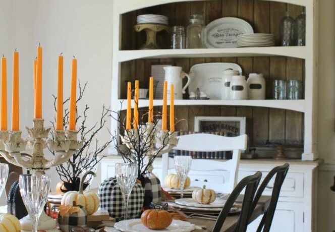 Mini trees covered in black glitter work as the centerpiece display, while small pumpkins and checkered pumpkins made from material scraps line the middle of the table. Orange tapered candlesticks add some height to the tablescape