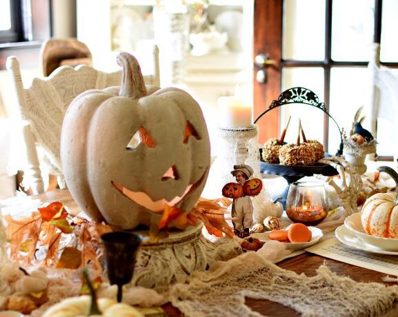 A large terra cotta pumpkin figure takes pride of place on a table covered by vintage Halloween cards and handmade cobwebs made from old throws