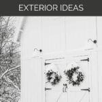 White barn with snowy farmhouse exterior and wreaths on doors and text