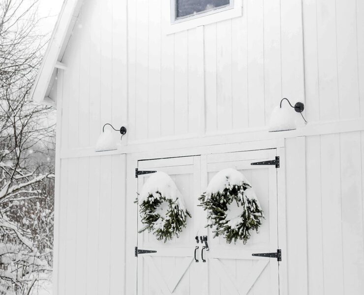 White barn with snowy farmhouse exterior and wreaths on doors