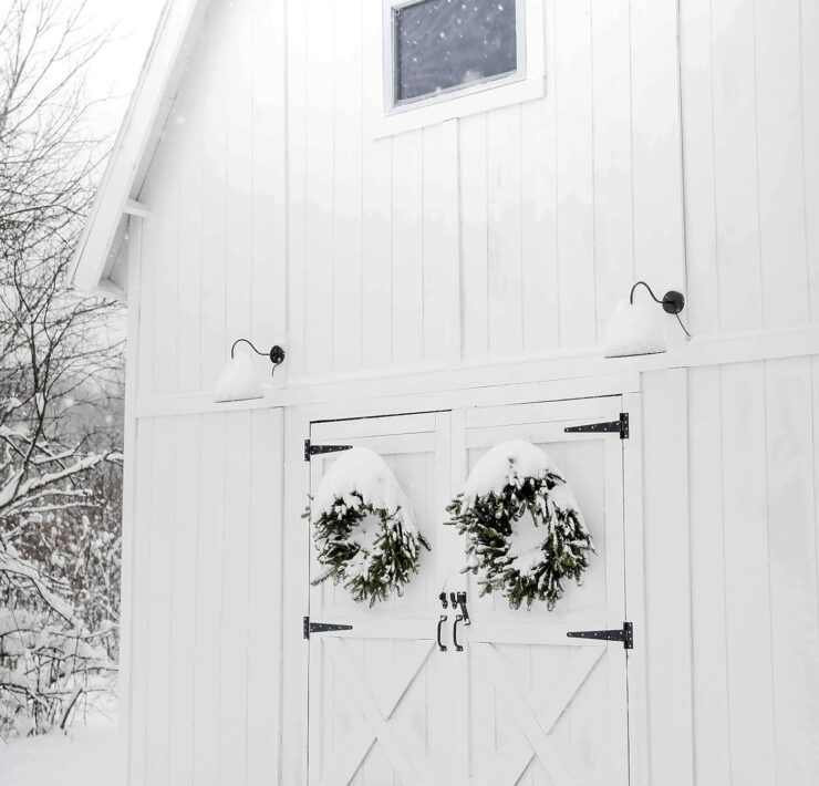 White barn with snowy farmhouse exterior and wreaths on doors