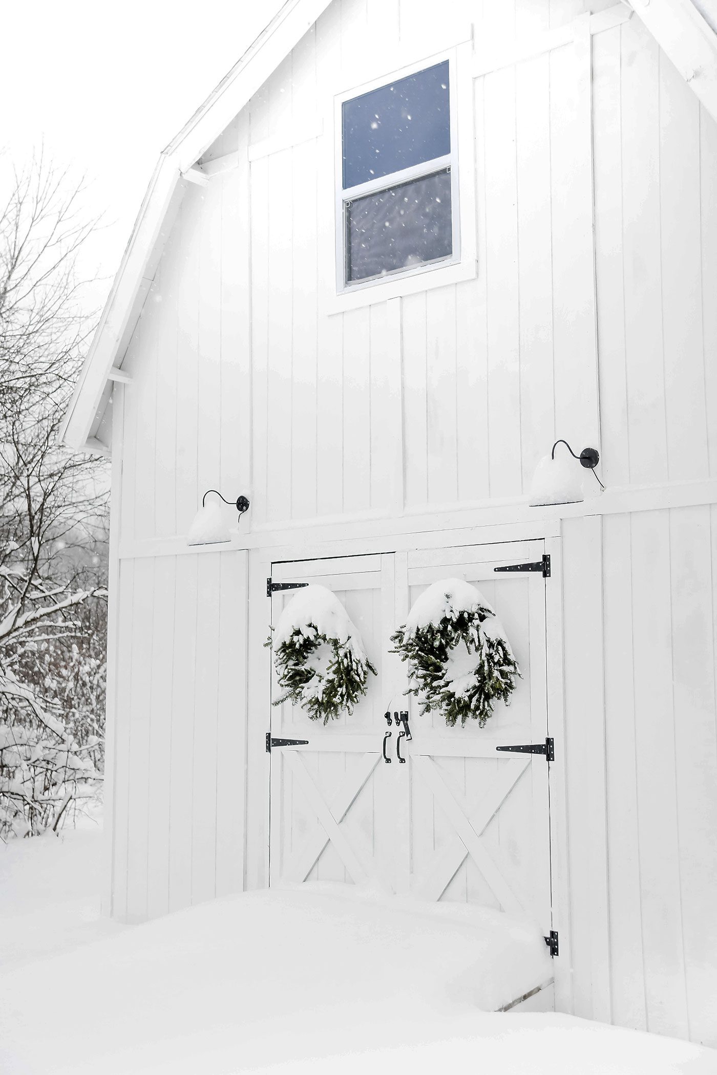 White barn with snowy farmhouse exterior and wreaths on doors