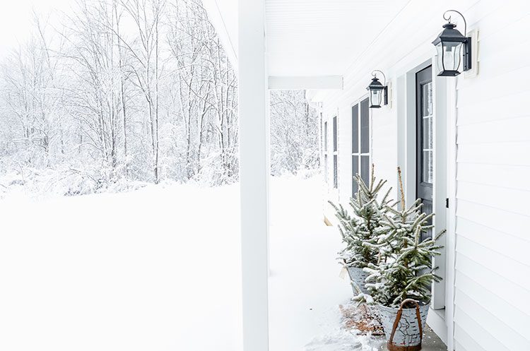 Front porch in the snow with trees outside front door of farmhouse wis sow on them