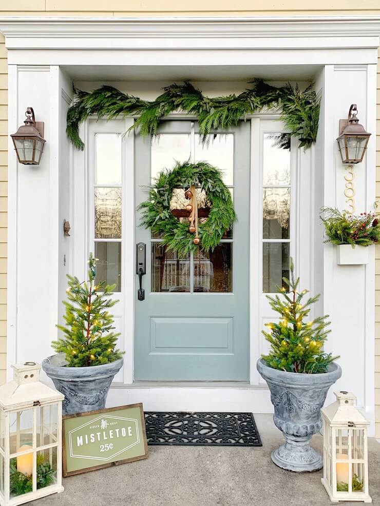 A blue door framed by green wreaths and garland with stone vases in front.