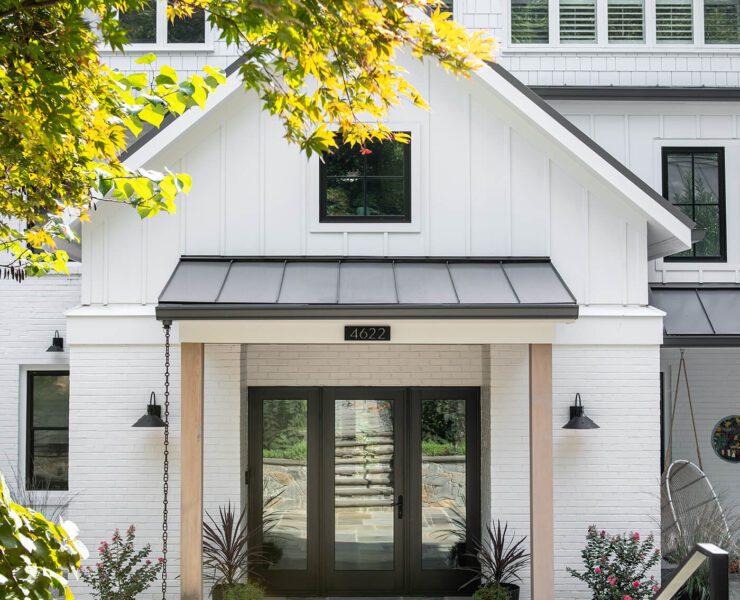 The exterior of a modern farmhouse style home with white paint, wood beams, and a black roof.