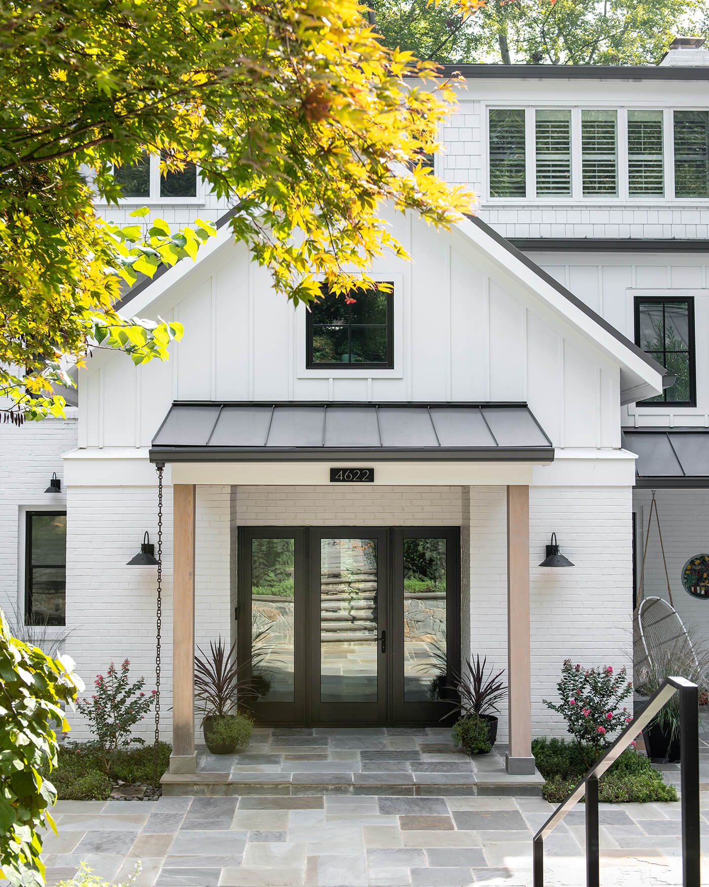 The exterior of a modern farmhouse style home with white paint, wood beams, and a black roof.