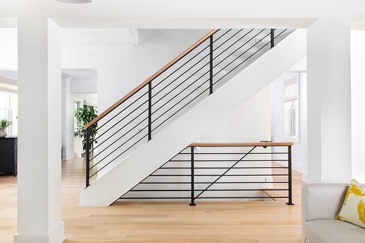 A mostly white interior with dark metal stairwell railing and a wood bannister.