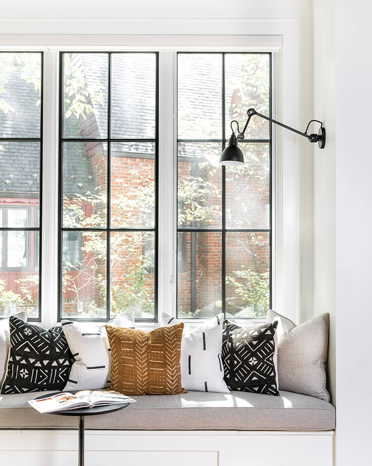 Afro-Cuban print pillows sit on a gray window nook with farmhouse style black window frames.