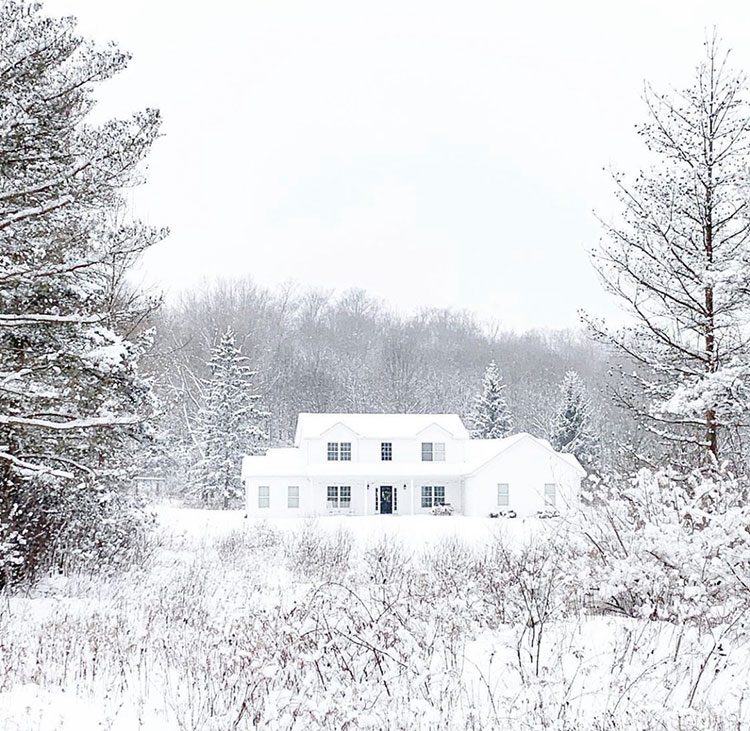 Exterior of white farmhouse with snowy farmhouse vibes in New York countryside and pine trees surrounding house