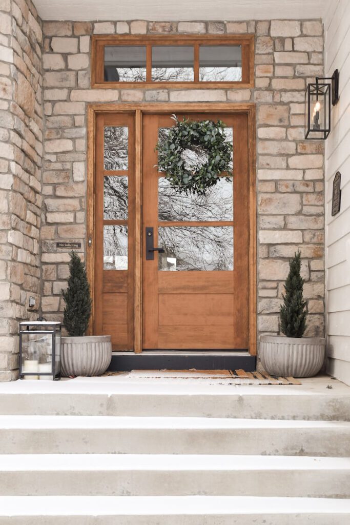 Steps lead up to a stone porch centered on a wood door with two small plants on either side.