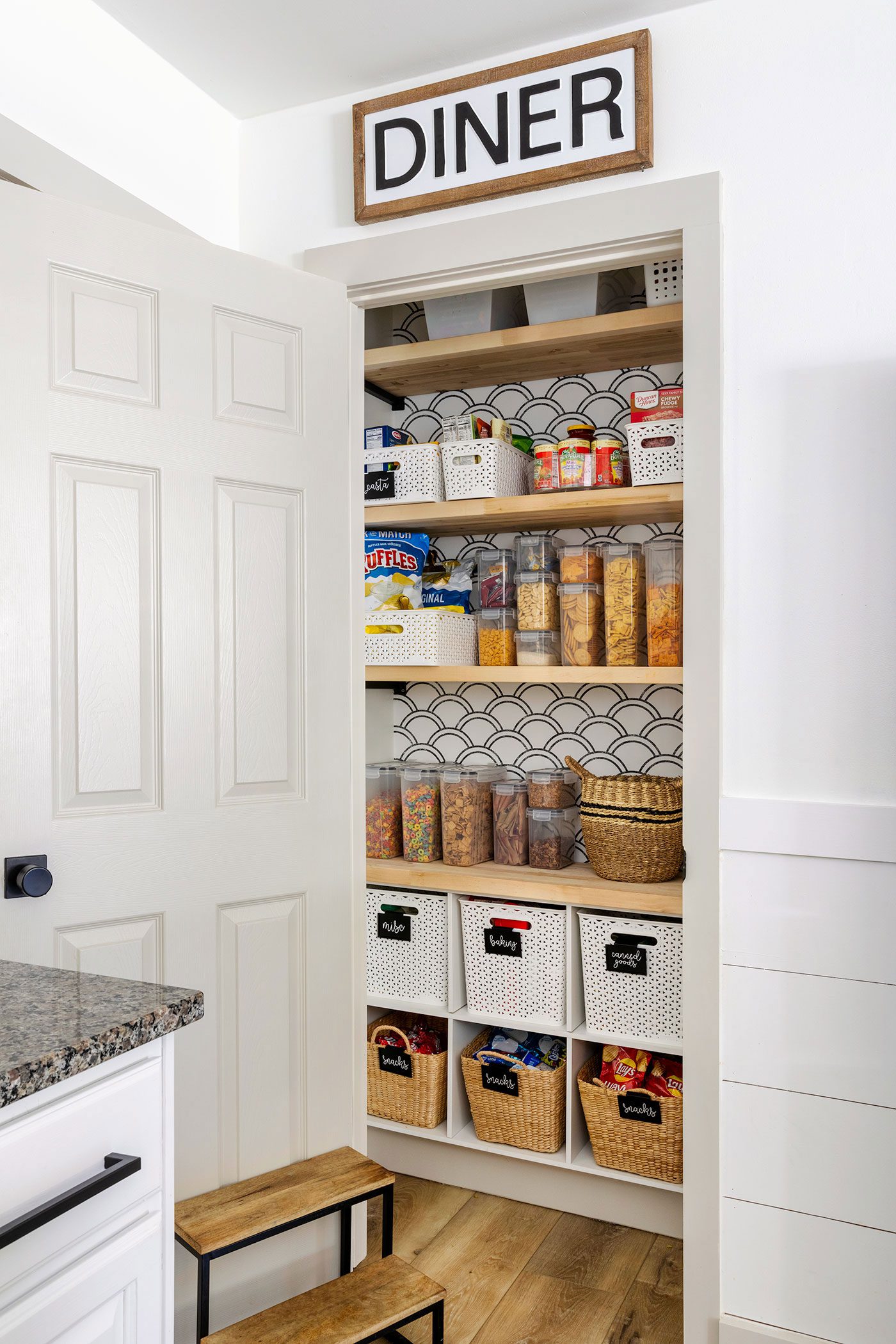 Open pantry door with wallpaper behind shelves and organized food