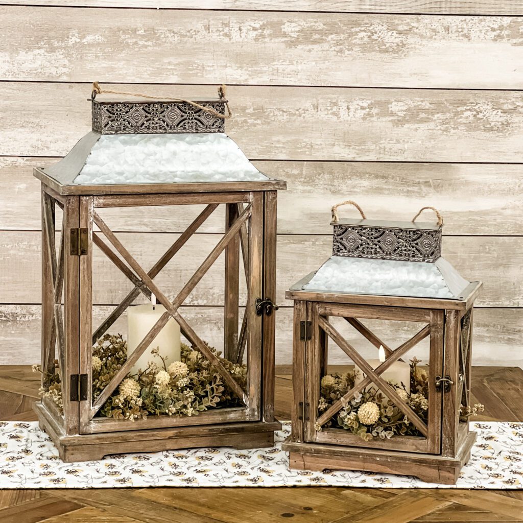 One small and one large Piper Classics wood lantern-style candle holders holding
dried flowers and one candle.