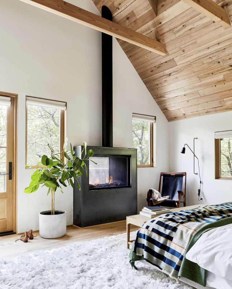 A black square wood burning stove with rustic appeal fits the MCM look and the farmhouse style decor of the striped bed sheets and shiplap wood ceiling
