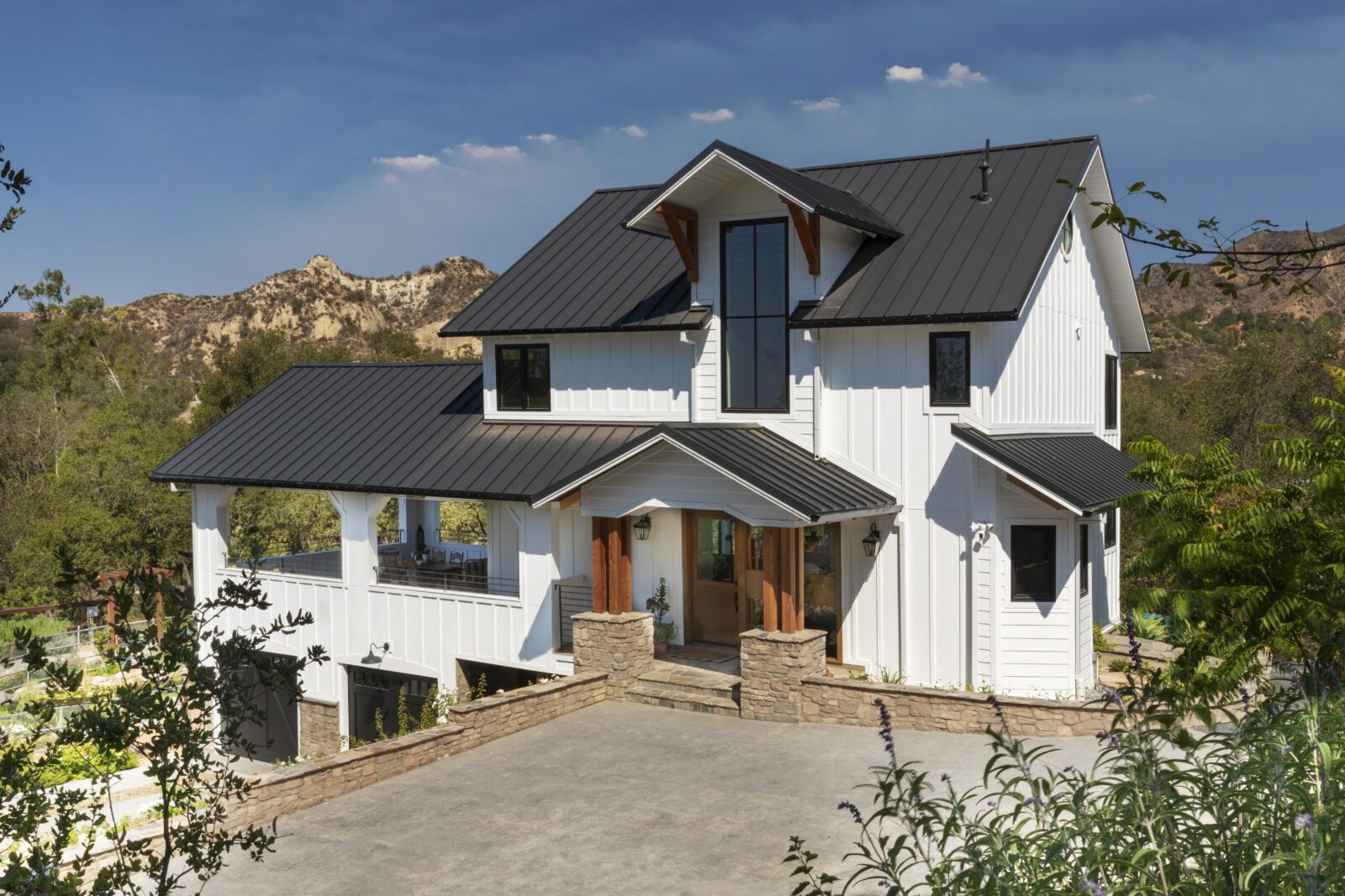 The remodeled exterior of the Farmhouse is warm and welcoming with white board and batten walls, a standing seam black metal roof, wooden ornamental trim including oversized exterior corbels and pillars and a gorgeous stained Dutch door.