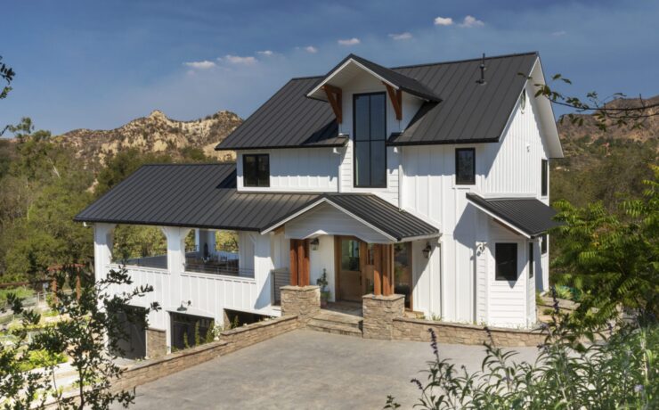 The remodeled exterior of the Farmhouse is warm and welcoming with white board and batten walls, a standing seam black metal roof, wooden ornamental trim including oversized exterior corbels and pillars and a gorgeous stained Dutch door.