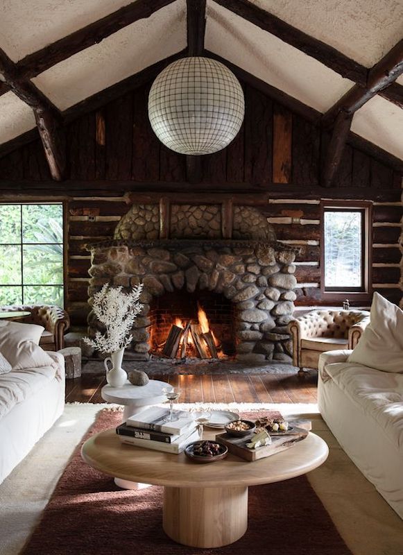 Large stones and dark wood logs make up the rustic style chimney of this rustic farmhouse. Darker shades make up the palette as well, with darker wood shades.