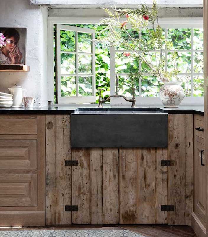 A rustic style wood is used for under the kitchen sink with a stone black apron farmhouse style sink